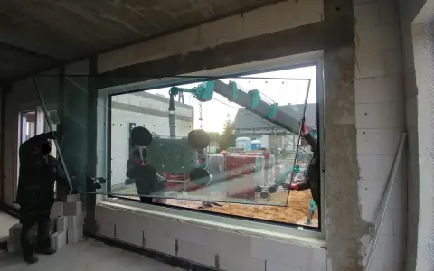 Pracownicy montują duże okno z użyciem dźwigu, zapewniając ciepły montaż okien.