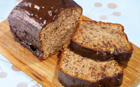 Saftiger Kuchen mit Bananen und Schokoladenglasur, auf einem Holzbrett serviert.