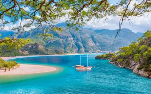 Malownicze widoki na turcja oludeniz: turkusowa woda, piaszczysta plaża i góry. Statek kołysze się na falach.