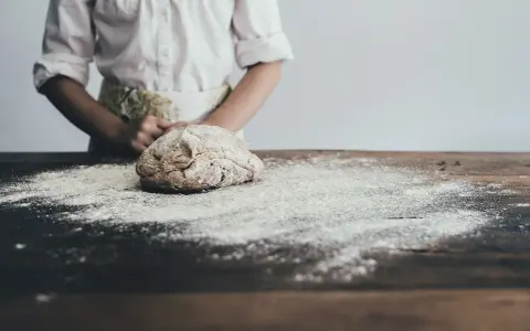 Dziecko w fartuszku przygotowuje masę solną. Na drewnianym stole rozsypana mąka, idealna do lepienia.