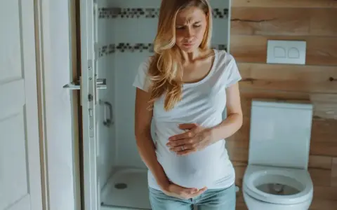 Kobieta w ciąży z wyrazem bólu na twarzy trzyma się za brzuch. Może to być ból podbrzusza w ciąży.