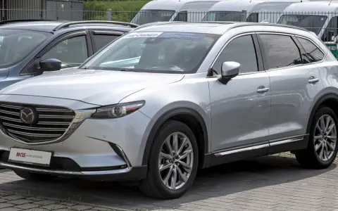 Srebrna Mazda CX-9 z napisem "PRE-OWNED" na przedniej szybie, zaparkowana na zewnątrz.