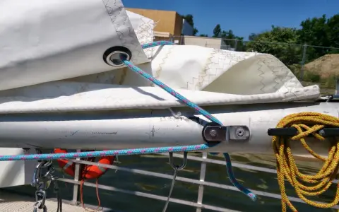 Poulie pour prise de ris automatique sur un mât de bateau, avec des cordages bleus et roses.