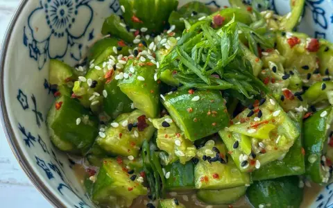Erfrischender asiatischer Gurkensalat mit Sesam, Chili und Frühlingszwiebeln in einer blumengemusterten Schüssel.