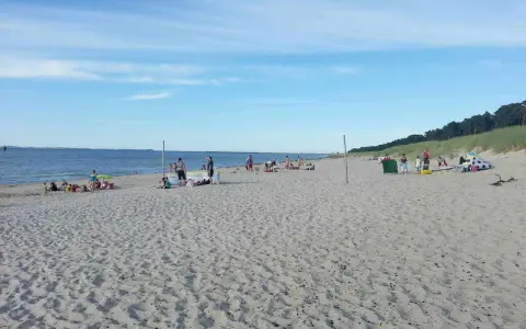 Menschen entspannen sich am sonnigen Lubmin Strand. Das Meer glitzert, der Himmel ist blau mit leichten Wolken.