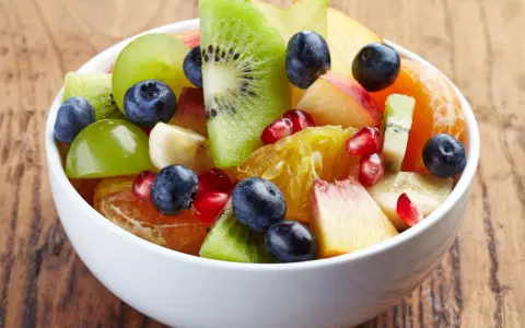 Kolorowa sałatka owocowa zimowa: kiwi, pomarańcza, winogrona, borówki, granat i brzoskwinia w białej misce.