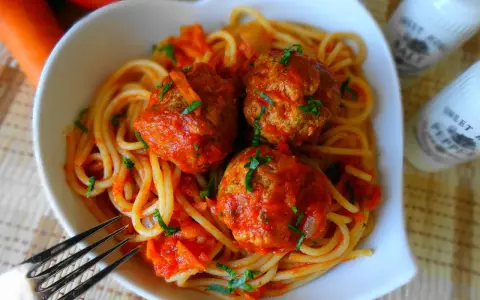 Pyszne spaghetti z klopsikami w sosie pomidorowym, posypane natką pietruszki. Idealne danie dla całej rodziny.