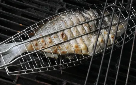 Ein ganzer Fisch wird in einem Grillkorb gegrillt. Die Haut ist goldbraun und leicht gebräunt.