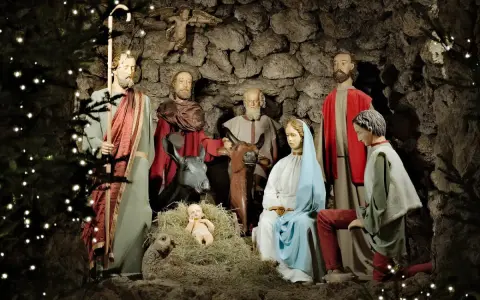 Pasterka w szopce: Święta Rodzina, pasterze i zwierzęta w grocie, ozdobionej światełkami.