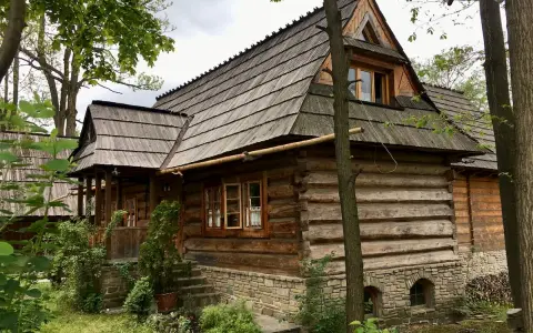 Drewniana chata z kamiennym fundamentem, kryta gontem, otoczona zielenią. Ulica Kościeliska w Zakopanem zachwyca tradycyjną architekturą.