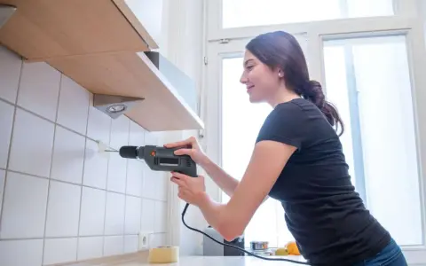 Frau bohrt mit Bohrmaschine ein Loch in die geflieste Wand, um ein Regal zu befestigen.