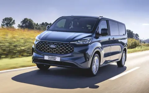 Ciemnoniebieski ford 7 osobowy Tourneo Custom pędzi po drodze wśród pól.