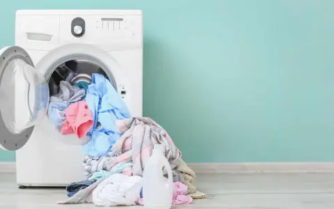 Lavadora blanca con ropa de colores y botella de detergente. Aprende como limpiar la lavadora para un mejor lavado.