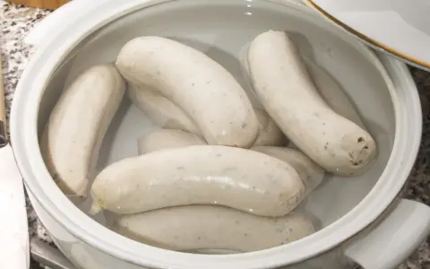 Biała kiełbasa w garnku z wodą, gotowa do parzenia. Delikatne kiełbaski czekają na idealny moment, by trafić na stół.