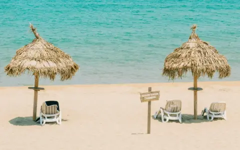 Idealna pogoda Tunezja wrzesień: dwa słomiane parasole i leżaki na piaszczystej plaży, turkusowe morze w tle.