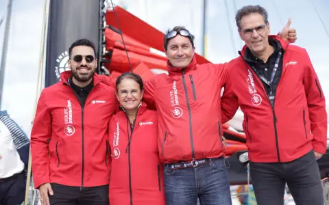Erwan Thiboumery et trois autres personnes souriantes portent des vestes rouges du Groupe Interaction, devant un bateau.