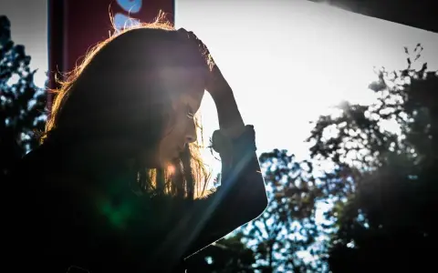 Kobieta z ręką na głowie, pogrążona w myślach. Słońce przebija się przez jej włosy, jakby szukała lekarstwa na zmartwienia.