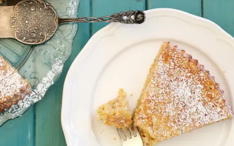 Saftige spanische Mandeltorte, bestäubt mit Puderzucker, auf einem weißen Teller. Ein Stück wurde bereits mit einer Gabel entnommen.