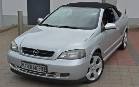 Silberner Opel Astra Bertone Cabrio mit offenem Verdeck, bereit für eine Spritztour.