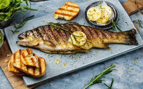 Perfekt gegrillte Forelle mit Kräutern, Zitronenscheibe und geröstetem Brot. Ein Genuss für jeden Fischliebhaber.