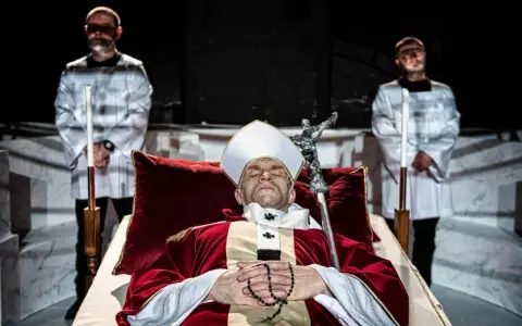 Papież w stroju, z różańcem, leży w trumnie. Obok stoją dwaj mężczyźni w białych szatach. Czy to bluźnierstwo, co to?