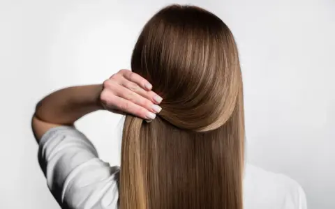 Capelli lisci e setosi, senza crespo, grazie a una routine efficace. La mano accarezza la chioma lucente.