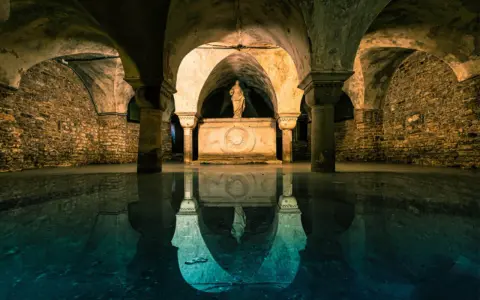 Un'antica cripta veneziana sommersa, con una statua su un altare e riflessi sull'acqua. Un tesoro nascosto di Venezia.