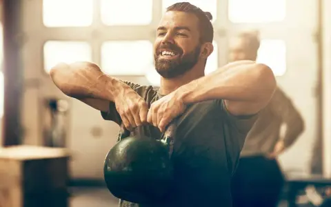 Un homme souriant effectue un exercice kettlebell, concentré sur son entraînement.