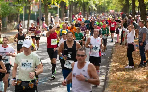 Läufer im Pulk auf einer Straße, einige mit Startnummern, die auf einen Marathon unter 4 Stunden hindeuten.