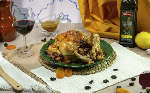 Pollo asado relleno, dorado y jugoso, servido en plato verde con pasas y orejones. Acompañado de vino tinto y aceite de oliva.