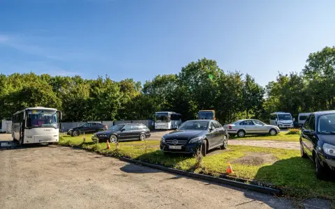 Na parkingu przy zamku Bolków stoi kilka samochodów i autobusów.