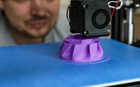 A man watches his 3D printer create a purple object, showcasing its precise 3D printer specifications in action.