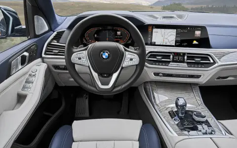 Wnętrze BMW X7: kierownica, ekran multimedialny z nawigacją i muzyką, panel klimatyzacji, dźwignia zmiany biegów.