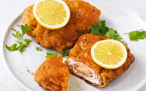 Zwei goldbraune Cordon Bleu mit geschmolzenem Käse und Schinken, garniert mit Zitronenscheiben und Petersilie.