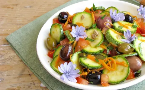 Insalata di zucchine fresca con pomodori, olive, carote e fiori di cicoria, un piatto colorato e leggero.