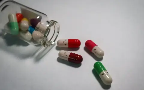 Kolorowe kapsułki, niektóre z uśmiechniętymi buźkami, wypadają z butelki. To mogą być psychotropy, które pomagają w trudnych chwilach.