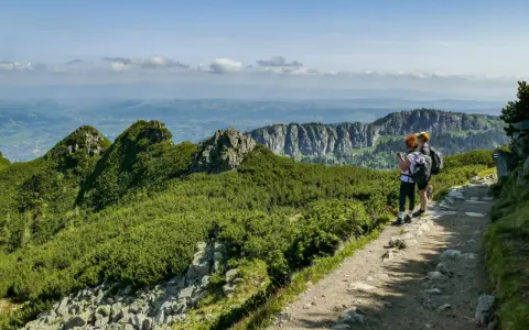 Dwie osoby z plecakami podziwiają widok na Tatry. Szlak jest kamienisty, ale stanowi łatwe zejście z Kasprowego Wierchu.