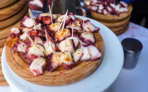 Pulpo a la gallega servido en tabla de madera, con palillos y espolvoreado con pimentón.