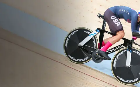 A determined track cyclist in a USA kit races on a wooden velodrome, pushing hard for victory.