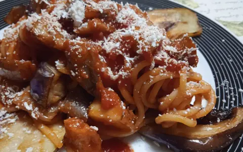 Un piatto invitante di pasta alla norma con melanzane fritte, sugo di pomodoro e ricotta salata grattugiata.