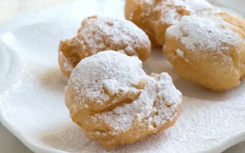 Vier goldbraune rheinische Krapfen, bestäubt mit Puderzucker, liegen auf einem weißen Teller.