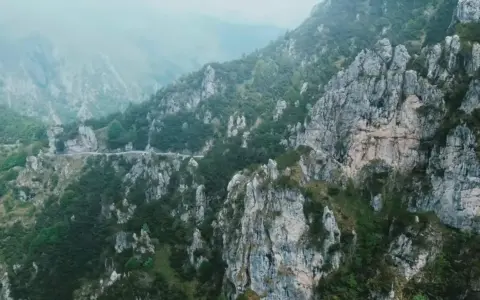 Strada tortuosa che sale verso il passo Barmone, tra rocce imponenti e vegetazione lussureggiante.