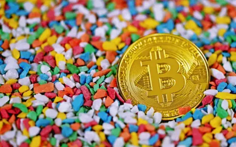 Złoty bitcoin wśród kolorowych kamyczków. Czy to symbol bogactwa, które James Howells stracił na zawsze?