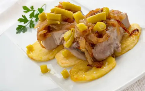 Bonito al horno sobre patatas, con cebolla caramelizada y pimientos verdes. Un plato delicioso y bien presentado.