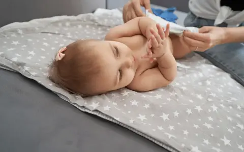 Bebé acostado en una manta con estrellas, mientras le cambian el pañal. Un paso más para dejar el pañal.