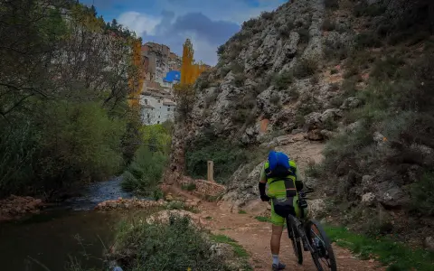 Ciclista en la ruta de las esculturas Bogarra, junto a un río y un pueblo en la ladera.