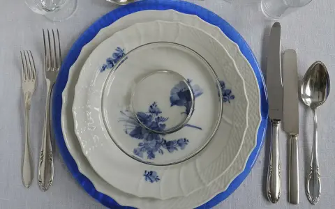 Vacker dukning med blå och vit porslin, bestick och glas. En elegant dessert tallrik väntar på att fyllas.