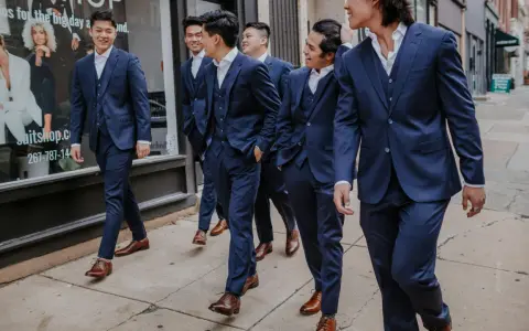 A group of men in navy suits walk down a sidewalk. They are all wearing brown dress shoes, proving you can wear brown shoes with a navy suit.