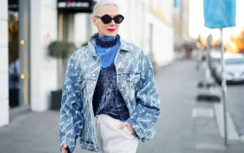 Kobieta w oversize'owej jeansowej katanie z nadrukiem, niebieskiej koszuli i błyszczącym topie.