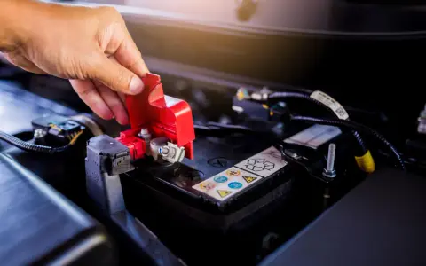 Mano che solleva il coperchio rosso di protezione del polo della batteria, un passo fondamentale per imparare come cambiare la batteria della macchina.
